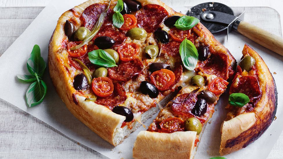 A deep dished pizza with tomatoes and basil