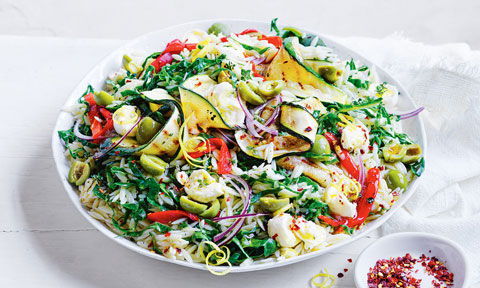 Antipasto salad with bocconcini, risoni, courgette ribbons and red capsicums served in a bowl with chilli flakes beside it