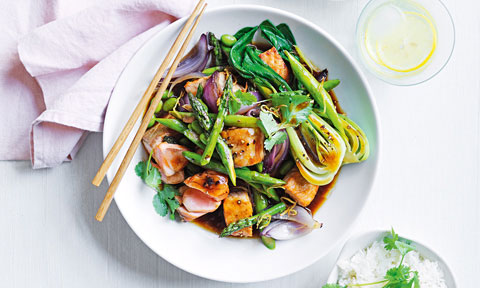 Asparagus, bok choy and salmon stir-fry in a bowl with chopsticks on the side