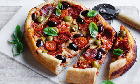 A deep dished pizza with tomatoes and basil