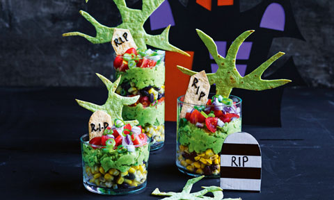 Thress cups of layered graveyard taco dips with writing icing tombstones