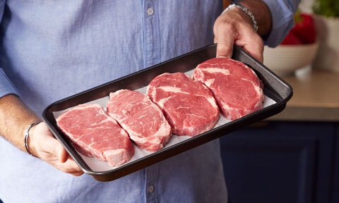 Four uncooked steaks in a baking dish