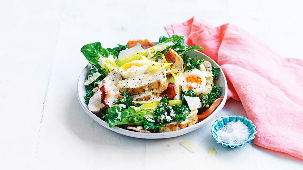 Chicken and kale caesar salad sprinkled with parmesan, aside with a small dish of salt