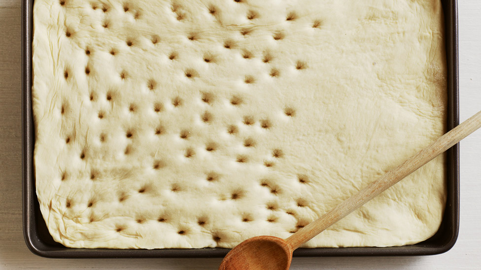 Uncooked focaccia douigh with a wooden spoon