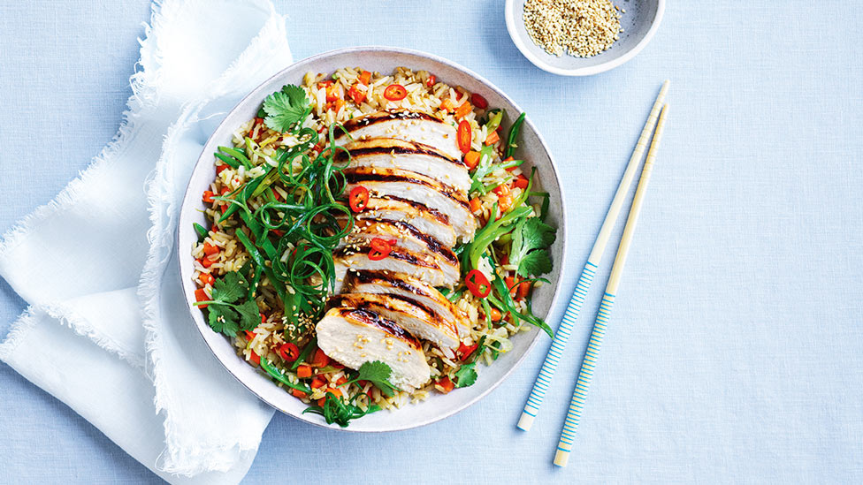 Fried rice with BBQ chicken and vegetables sprinkled with coriander, sesame seeds and spring onions, a pair of chopsticks aside