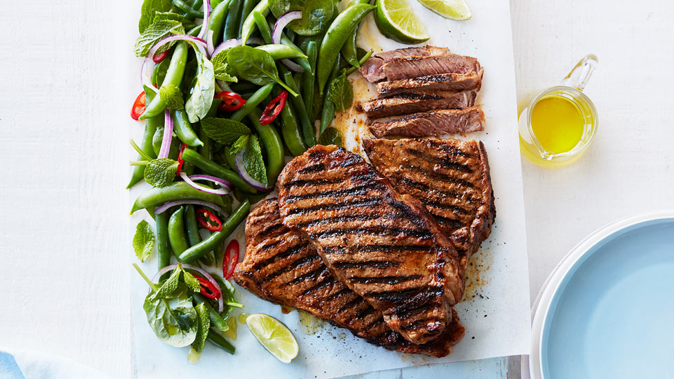 Three cuts of red curry steak with pea salad and lime wedges