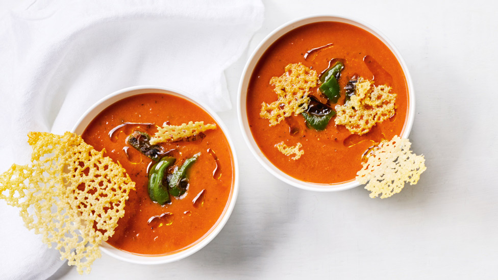 Two bowls of tomato and basil soup with chilli and parmesan crisps