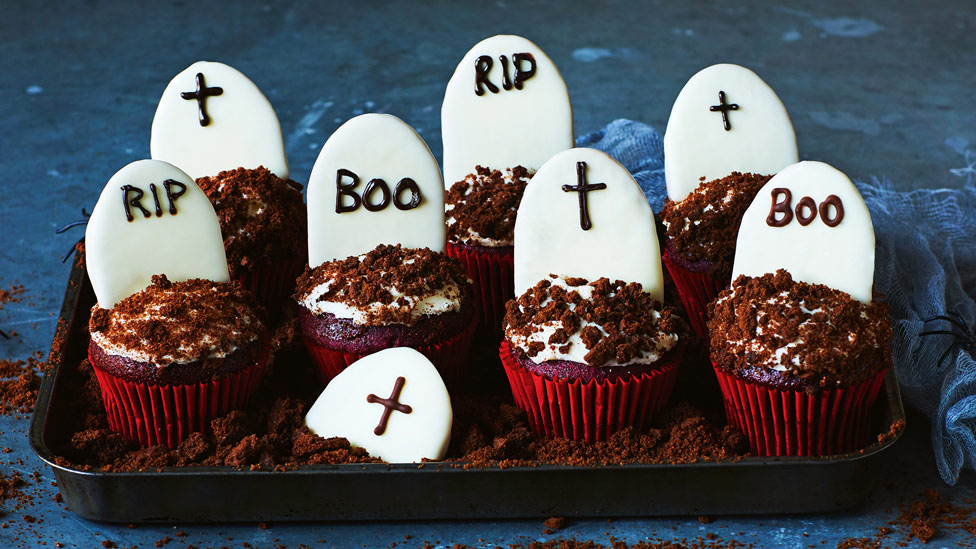 Seven tombstone cupcakes decorated with writing icing