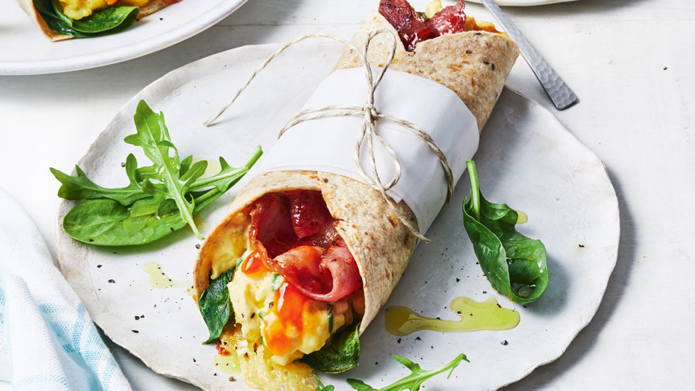 A breakfast burrito served on a plate with some rocket