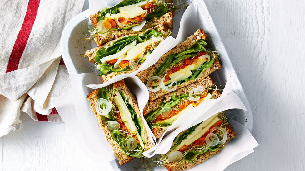 A lunch box with green salad sandwiches and hummus