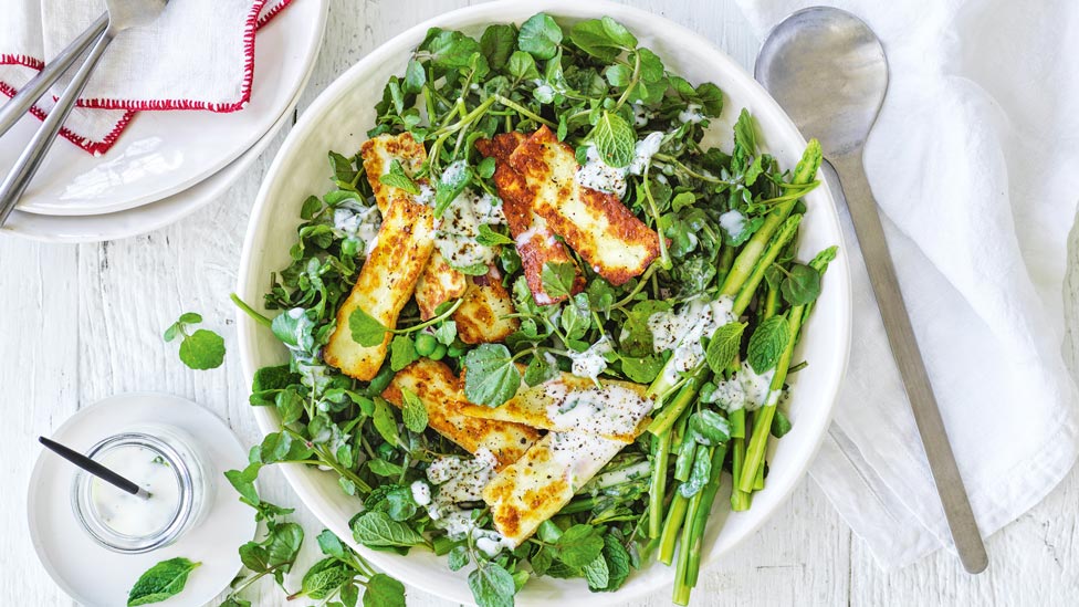 Grilled haloumi on top of green salad in a bowl