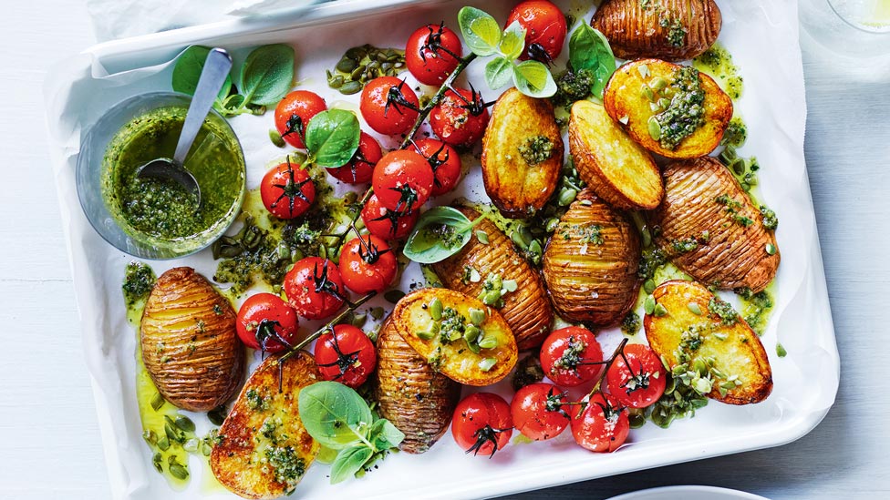 Tray of hasselback potatoes with roasted tomatoes and parsley pesto