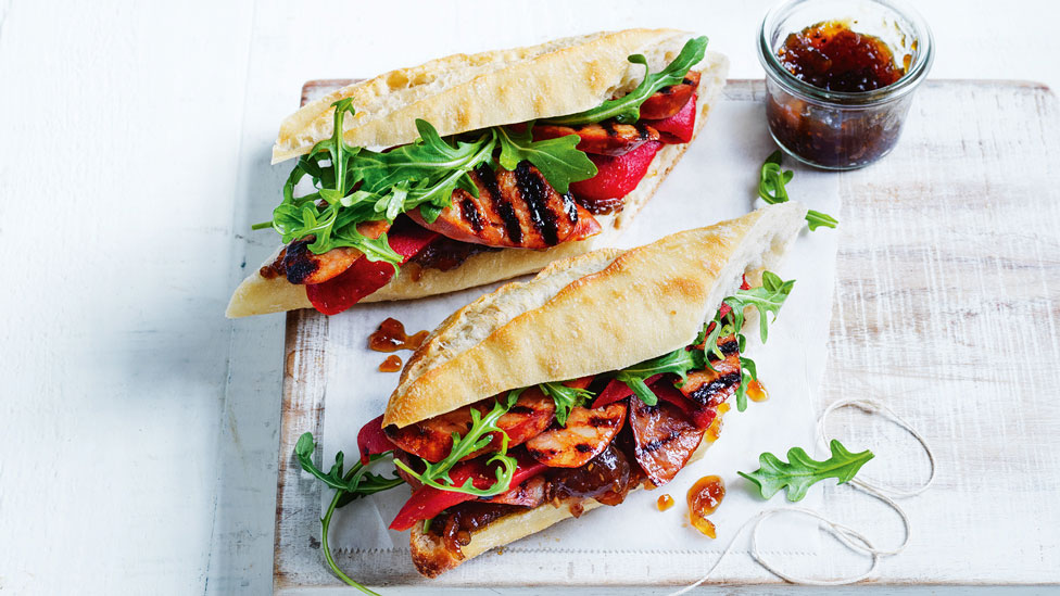 Two chorizo sandwiches on a chopping board stuffed with rocket