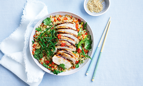 Fried rice with BBQ chicken and vegetables sprinkled with coriander, sesame seeds and spring onions, a pair of chopsticks aside