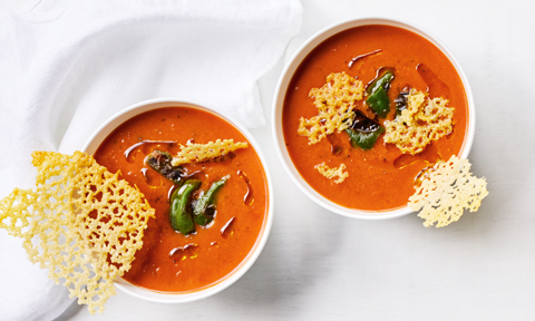 Two bowls of tomato and basil soup with chilli and parmesan crisps