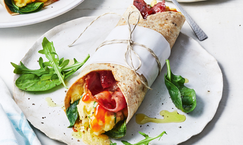 A breakfast burrito served on a plate with some rocket
