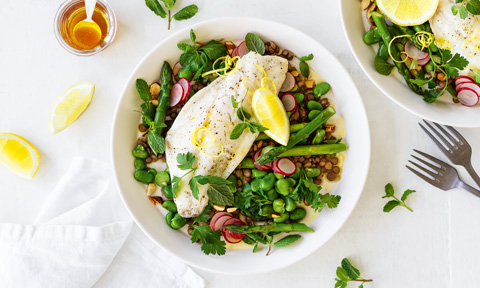 Steamed fish on top of broad bean and lentil salad with lemon wedges