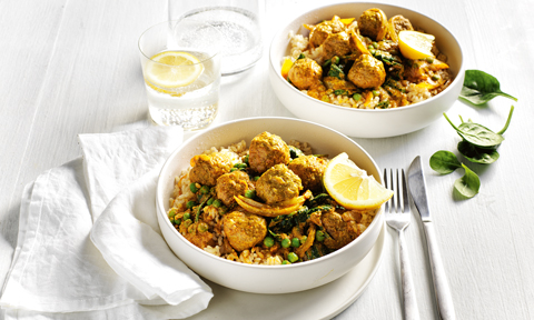 Two bowls of tikka meatball curry with lemon wedges