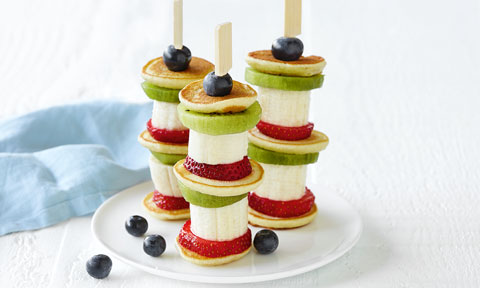 Three mini banana pancake stacks with kiwifruit, strawberry and blueberries