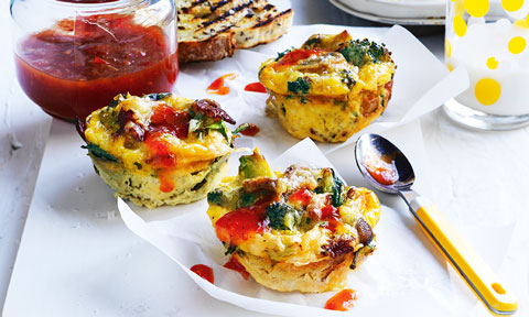 Three bacon and egg breakfast muffins on baking paper with a jar of salsa served beside
