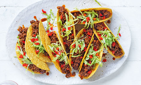 8 beef tacos on a plate topped with shredded lettuce and red capsicum