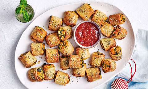 Gluten-free sweet potato and fetta sausage rolls on a serving platter with tomato sauce in the middle