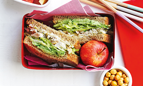 Green goodness sandwich cut in half and served in a lunch box with an apple