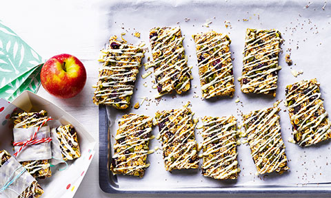 Muesli bars arranged on a tray with yogurt drizzle and an apple on the side