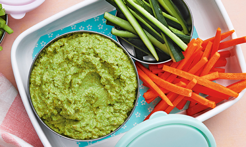 Pea hommus served in a bowl with cucumber and carrot sticks 
