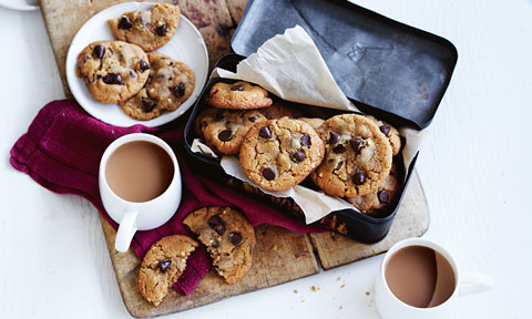 Peanut butter and choc chip cookies served in a baking tin with a cup of tea beside