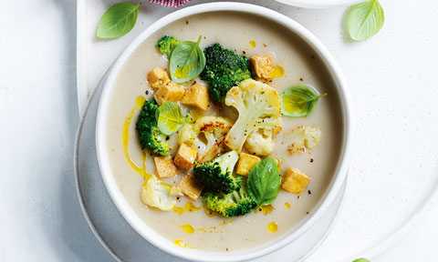Cauliflower and broccoli soup served in a bowl with croutons and basil