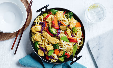 Satay chicken stir-fry served in a wok with noodles, broccoli and red peppers