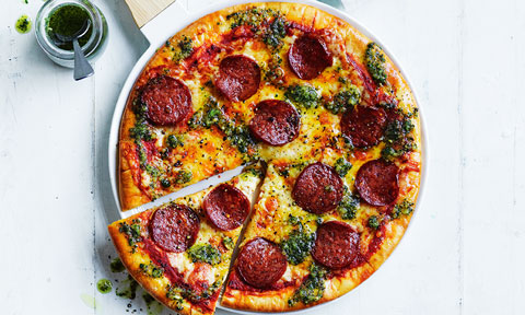 Whole pesto and pepperoni pizza with one slice cut out