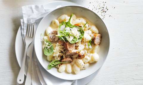 Gnocchi served in a bowl with spinach, sausage and parmesan cheese on top