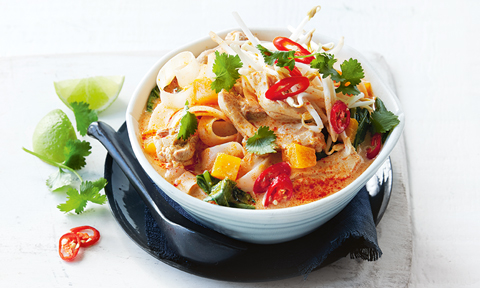 Chicken laksa in a bowl with bean sprouts, chilli and coriander with lime wedges on the side
