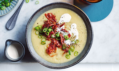 Potato and ham soup served in a bowl topped with spring onions and cream
