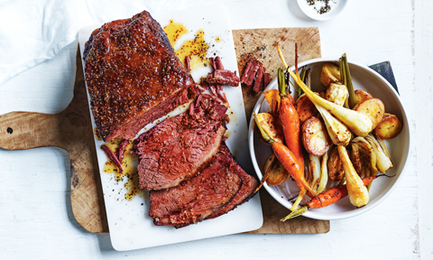 Corned beef served on a chopping board with a bowl of roast veggies beside