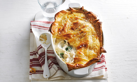 Whole chicken and mushroom pie served in a baking dish on top of a tea towel and serving spoon