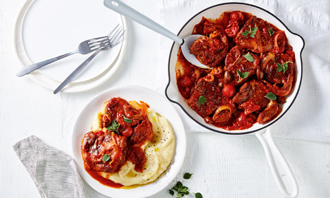Braised lamb served in a baking dish next to a plate of lamb with mashed potato