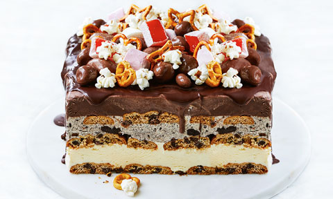 Ice-cream cake on a cake stand topped with popcorn, pretzels and turkish delight