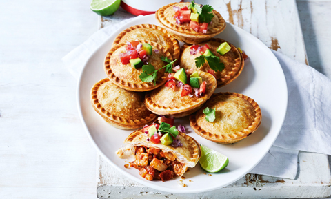 Mexican chicken pies stacked on a plate with avocado on top and lime wedge on the side