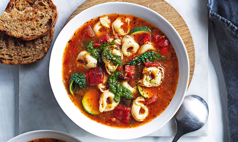 A bowl of ratatouille soup with cheese tortellini and bread on the side