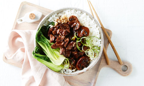 Sticky slow cooked beef served a bowl with rice and bok choy with chop sticks on the side