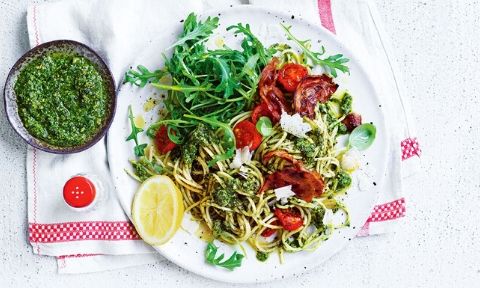 Pesto pasta served with tomato and pancetta with a lemon wedge on  the side