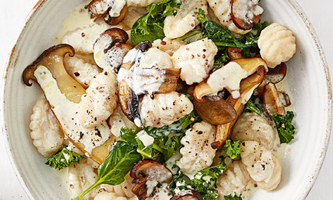Mushrooms and kale tossed with gnocchi and cream served in a bowl