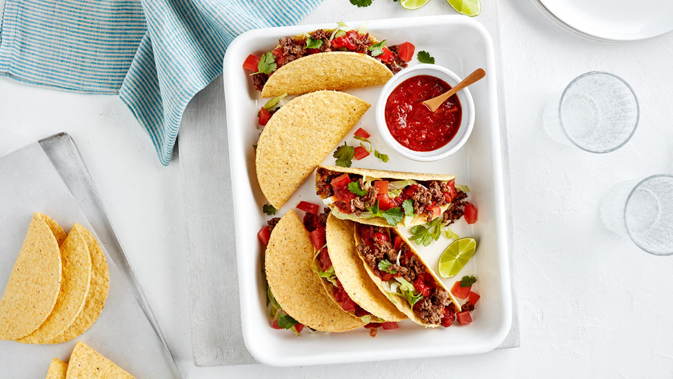 Mexican tacos stacked in a dish with salsa and lime wedges 