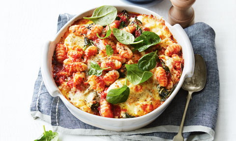 Ricotta and Spinach Gnocchi Bake in a baking dish, topped with spinach leaves