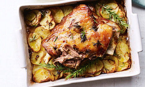 Roast Lamb with Mint Jelly Glaze garnished with rosemary. Laying on thinly sliced roast potatoes in the oven dish.