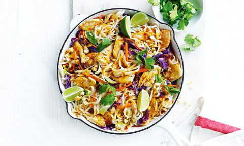 Dish with Thai-style chicken and noodle stir-fry, with lime wedges and a side bowl of coriander sprigs