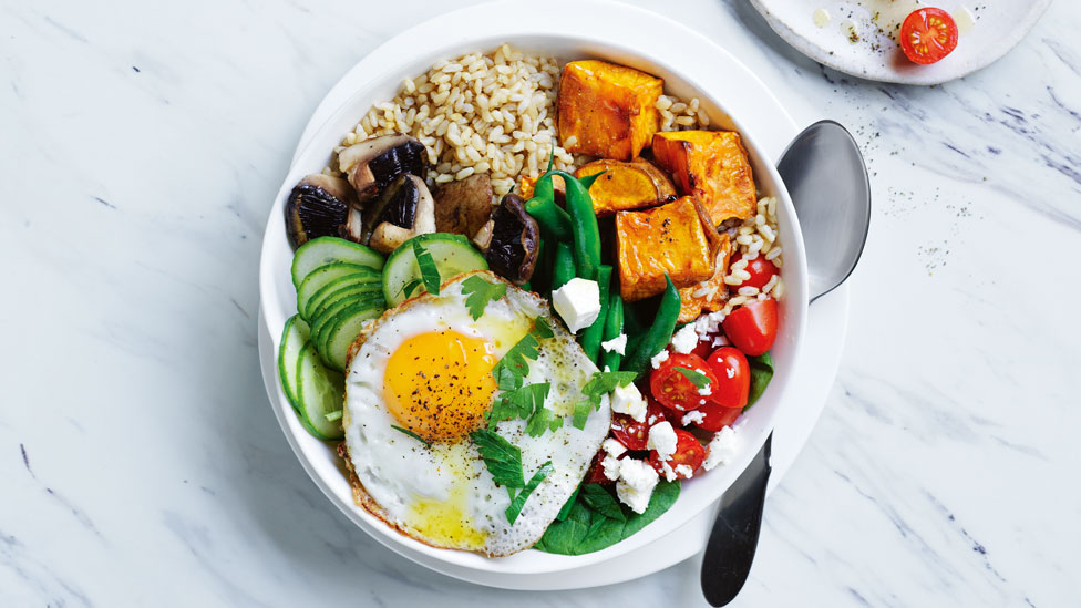 A dinner bowl of leftover meat, egg, veggies, grains and cheese